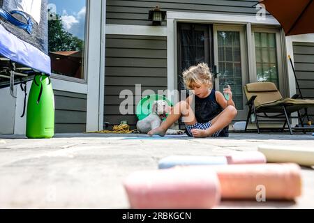 fille assise sur le sol dans l'arrière-cour jouant avec de la craie Banque D'Images