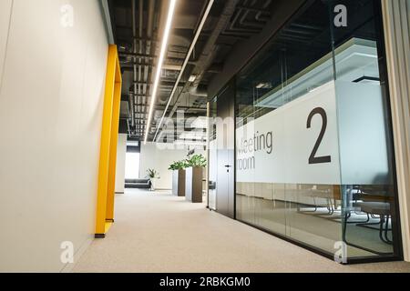 long et large couloir avec éclairage led, plantes vertes, salle de réunion derrière un mur transparent en verre dans un environnement de coworking moderne avec une technologie de pointe Banque D'Images