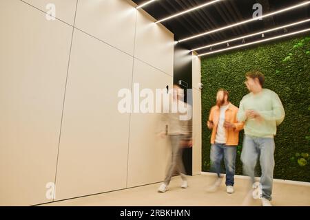 flou de mouvement de partenaires commerciaux créatifs marchant le long du couloir dans un espace de coworking moderne avec intérieur high tech, parler et planifier des affaires proj Banque D'Images