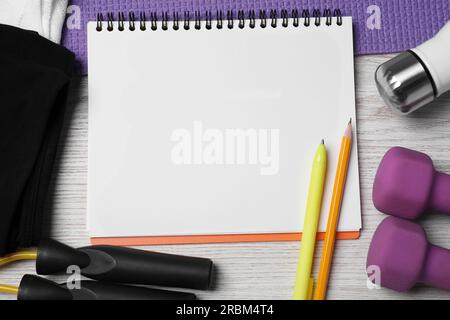 Cahier entouré d'équipements sportifs sur table en bois blanc, plat. Entraînement personnel Banque D'Images