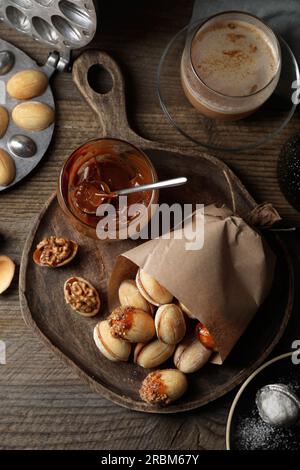 Biscuits faits maison en forme de noix fraîchement cuits, lait concentré bouilli et tasse de café sur la table en bois, plat Banque D'Images