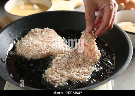 Schnitzel de cuisson. Femme mettant la côtelette de porc crue dans la chapelure dans la poêle, gros plan Banque D'Images