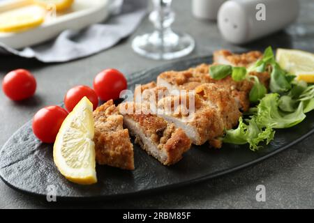 Savoureux schnitzel coupé servi avec des tomates, des légumes verts et du citron sur la table grise, gros plan Banque D'Images