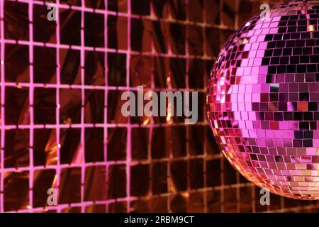 Boule disco brillante contre le rideau de fête de papier aluminium sous la lumière rose, espace pour le texte Banque D'Images