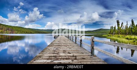 Beau lac de montagne avec reflet et jetée en bois. Nuages blancs moelleux et ciel bleu reflété dans l'eau calme Banque D'Images