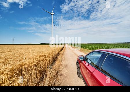 Paysage rural avec des éoliennes, route de campagne parmi les champs de cultures et voiture rouge Banque D'Images