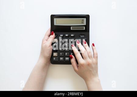 Calculatrice noire dans les mains d'une femme sur fond blanc, vue de dessus. Banque D'Images