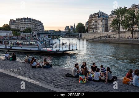 Paris romantique. Les gens, les étudiants au coucher du soleil avec bateau de croisière sur la rive gauche de la Seine dans le quartier Latin à socialiset. Quai de la Tournelle Paris. Banque D'Images