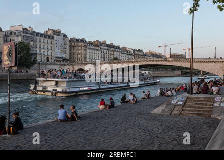 Les gens, les étudiants au coucher du soleil avec bateau de croisière sur la rive gauche de la Seine dans le quartier Latin à socialiset. Quai de la Tournelle par le pont de Tournelle. Paris. Banque D'Images