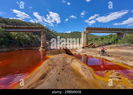 Belle femme avec vélo de montagne électrique sur un tour à vélo le long de la rivière Rio Tinto avec son eau rouge naturelle en Andalousie, Espagne Banque D'Images