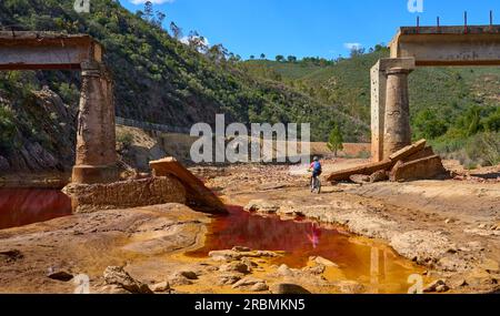 Belle femme avec vélo de montagne électrique sur un tour à vélo le long de la rivière Rio Tinto avec son eau rouge naturelle en Andalousie, Espagne Banque D'Images