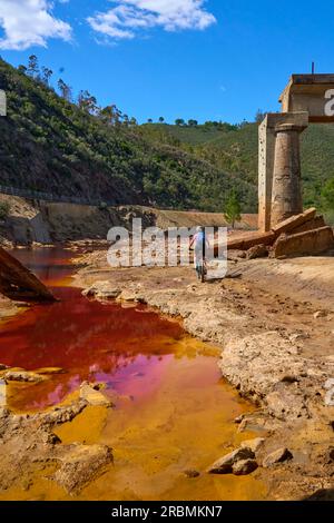 Belle femme avec vélo de montagne électrique sur un tour à vélo le long de la rivière Rio Tinto avec son eau rouge naturelle en Andalousie, Espagne Banque D'Images