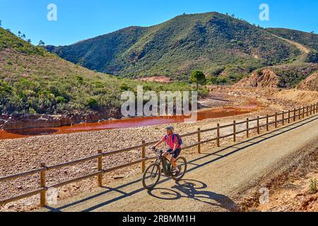 Belle femme avec vélo de montagne électrique sur un tour à vélo le long de la rivière Rio Tinto avec son eau rouge naturelle en Andalousie, Espagne Banque D'Images