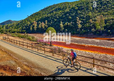 Belle femme avec vélo de montagne électrique sur un tour à vélo le long de la rivière Rio Tinto avec son eau rouge naturelle en Andalousie, Espagne Banque D'Images