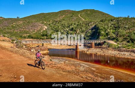 Belle femme avec vélo de montagne électrique sur un tour à vélo le long de la rivière Rio Tinto avec son eau rouge naturelle en Andalousie, Espagne Banque D'Images