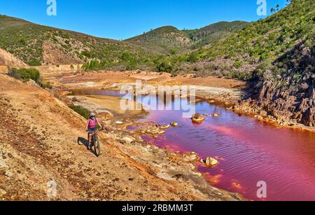 Belle femme avec vélo de montagne électrique sur un tour à vélo le long de la rivière Rio Tinto avec son eau rouge naturelle en Andalousie, Espagne Banque D'Images