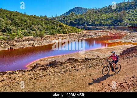 Belle femme avec vélo de montagne électrique sur un tour à vélo le long de la rivière Rio Tinto avec son eau rouge naturelle en Andalousie, Espagne Banque D'Images