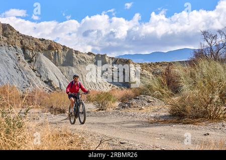 Belle femme senior active avec son vélo de montagne électrique sur un sentier dans le désert de Tabernas près d'Almeria, Andlusia, Espagne Banque D'Images