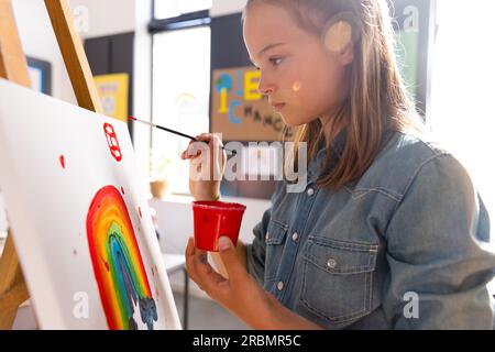 Peinture d'écolière caucasienne au pinceau et au chevalet en classe d'art scolaire Banque D'Images