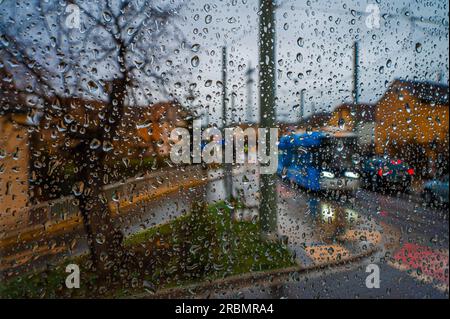 Gouttes de pluie sur une vitre donnant sur une intersection avec des voitures en mouvement et un tram, Iéna, Thuringe, Allemagne Banque D'Images