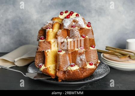 Prendre une tranche de délicieux gâteau de Noël Pandoro avec sucre en poudre et baies sur table noire Banque D'Images