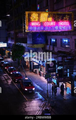 Hong Kong, Chine - avril 28 2023 : lumière néon colorée signe d'un hôtel et ligne de taxi rouge la nuit sur Lockhart Road Banque D'Images