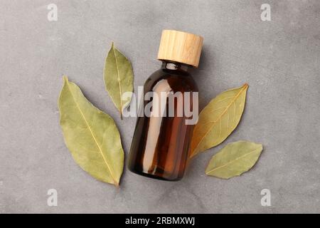 Bouteille d'huile essentielle de Laurier et feuilles séchées sur table gris clair, mise à plat Banque D'Images