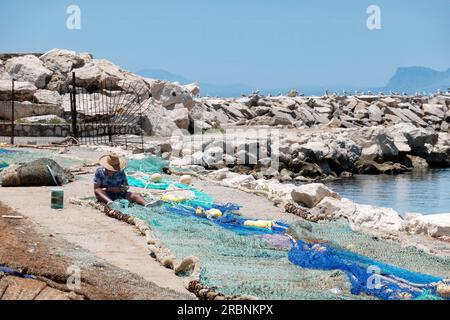 Un pêcheur réparant ses filets de pêche du côté du quai du port de pêche. Le port est situé à Estepona en Espagne avec Gibraltar en arrière-plan Banque D'Images