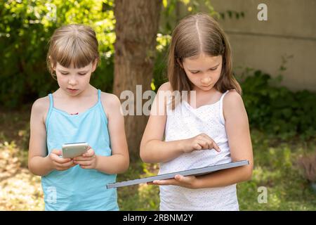 Deux filles en âge de fréquenter l'école primaire tenant, à l'aide d'appareils électroniques, une calculatrice et un clavier. Concept publicitaire pour enfants et électronique, photo en plein air. Deux peo Banque D'Images