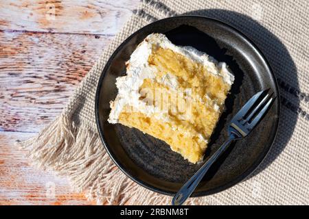 Une seule portion plaquée d'un gâteau de meringue au citron fait maison servi à une table plaquée. le gâteau a une garniture au citron caillé et un glaçage à la crème au beurre Banque D'Images