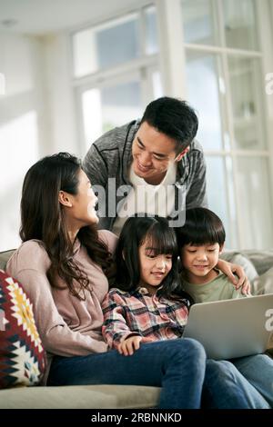 jeune couple asiatique et deux enfants assis sur le canapé de la famille à la maison regardant un film ensemble à l'aide d'un ordinateur portable Banque D'Images