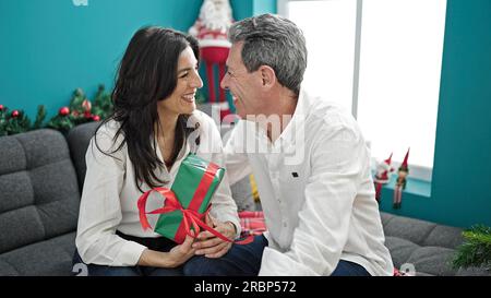 Homme senior et femme couple tenant le cadeau de noël assis sur le canapé à la maison Banque D'Images