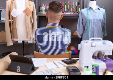 Homme hispanique avec couturier barbe travaillant dans un atelier debout en arrière regardant loin avec les bras croisés Banque D'Images