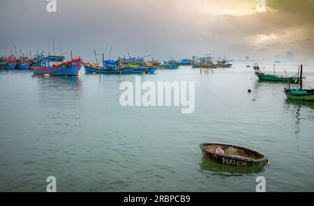 Un coracle abandonné et des bateaux de pêche en bois amarrés sous la pluie à Thọ Quang, Sơn Trà, Danang, Vietnam Banque D'Images