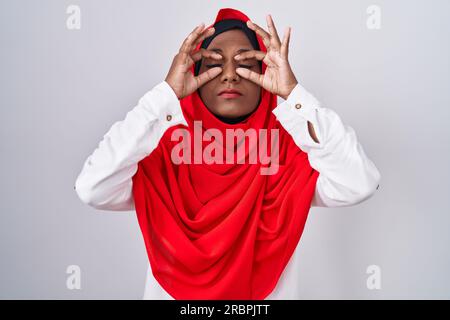 Jeune femme arabe portant le foulard traditionnel islamique du hijab essayant d'ouvrir les yeux avec les doigts, somnolente et fatiguée pour la fatigue matinale Banque D'Images