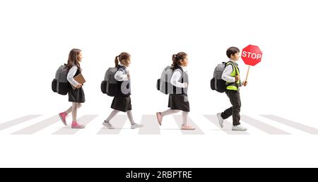 Photo de profil en longueur d'un groupe d'enfants traversant une rue et portant un panneau de signalisation d'arrêt isolé sur fond blanc Banque D'Images