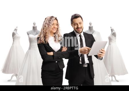 Homme professionnel dans un costume noir montrant une tablette numérique à une femme d'affaires dans un magasin de mariée isolé sur fond blanc Banque D'Images