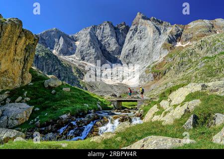 Homme et femme marchant sur le pont au-dessus de la crique, Vignemale en arrière-plan, Vallée de Gaube, Gavarnie, Parc National des Pyrénées, Pyrénées, France Banque D'Images