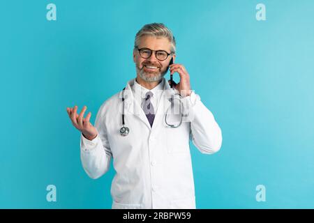 Sympathique beau médecin ont l'appel téléphonique avec le patient, fond bleu Banque D'Images