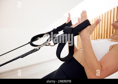 Femme flexible mince fait Pilates sur un lit reformeur dans un studio lumineux. Vue rapprochée de ses mains tenant des sangles tendues. lif sain Banque D'Images