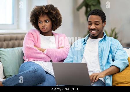 Bouleversé jeune femme noire solitaire assise par son mari à l'aide d'un ordinateur portable Banque D'Images