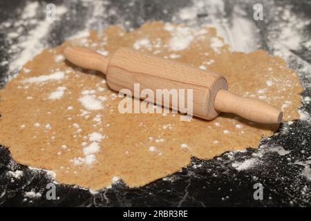 un rouleau à pâtisserie repose sur une pâte à biscuits qui a été étalée. La pâte est sur un comptoir saupoudré de farine. Banque D'Images