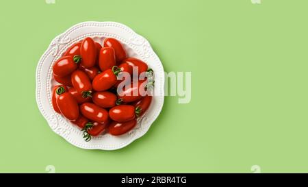 Tomates cerises rouges Ornela sur une assiette blanche sur fond vert. Tas de tomates en forme de petite bouteille sur une assiette. Légumes bio nourriture végétarienne Banque D'Images