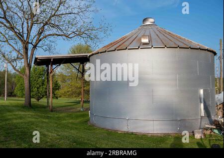 Stockage et séchoir d'alimentation en soja à grain ondulé en acier inoxydable excentré sous un ciel bleu sur un champ agricole herbeux. Pas de personnes, avec espace de copie. Acric Banque D'Images