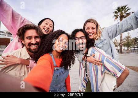 Groupe heureux d'amis qui s'amusent en plein air, qui font du pigeyback tout en prenant un selfie pour les médias sociaux. Banque D'Images