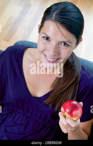 Portrait d'une belle jeune femme montrant un juteux frais pomme rouge dans sa main tandis qu'elle favorise une saine alimentation biologique Banque D'Images