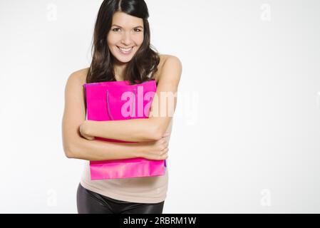 Exalté jeune femme serrant ses achats dans un joli sac à provisions violet près de sa poitrine d'une manière possessive comme elle sourit joyeusement montrant Banque D'Images