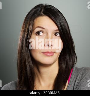 Femme attrayante avec une expression sceptique bémused debout avec les bras pliés tirant un visage circonspect alors qu'elle regarde vers le haut dans les airs Banque D'Images