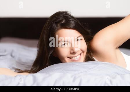 Femme en bonne santé rafraîchie après une bonne nuit de sommeil s'étendant dans le lit et souriant à la caméra en plaisir et satisfaction Banque D'Images