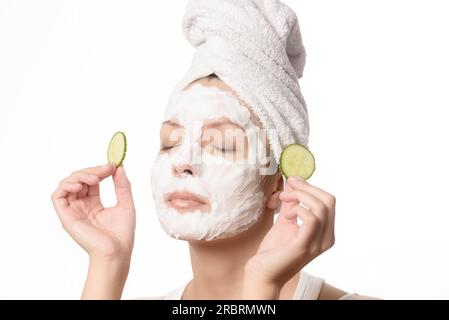 Femme souriante avec ses cheveux attachés dans une serviette blanche et un masque facial nourrissant nettoyant en profondeur appliqué sur sa peau tenant une tranche rafraîchissante de Banque D'Images